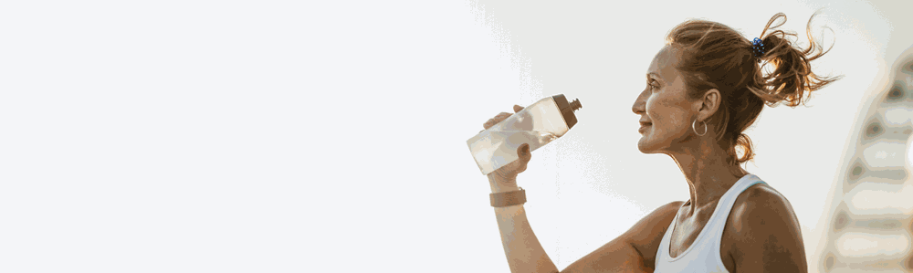 A woman in her 50s drinking water outdoors after a workout